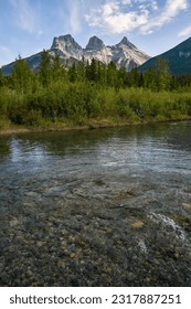 ゴールデンアワー、青空の日の日没、有名な観光地の山々の下の水面に映る穏やかで平和な午後、キャンモアのスリーシスターズのポートレートビュー、夏のエリア。