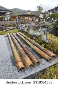 Fântână de apă japoneză și asiatică pentru purificarea corpului, cu ramuri de bambus, în jurul unui lac, cu robinete în formă de dragon legendar, sub un cer gri și înnorat, cer gri, înnorat și trist