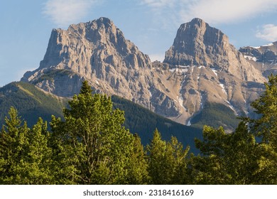 Three Sisters in Canmore seen in summer time sunset with mountain peaks shining bright with sunshine. Beautiful, pristine, famous, tourist area, Banff National Park.