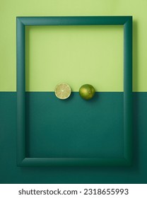 Whole and cut in half lime in wooden picture frame on two-tone green background