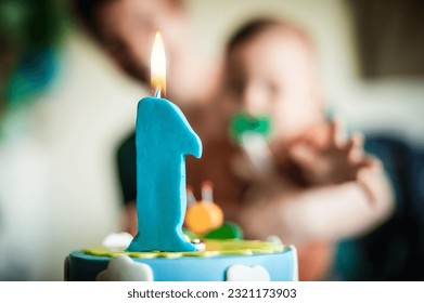 Un adorable petit garçon fête son premier anniversaire en famille à la maison. Gâteau et bougie en forme de chiffre un.