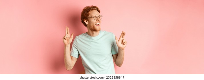 Cheerful redhead guy listening music and dancing, triumphing or celebrating success, standing over pink background.