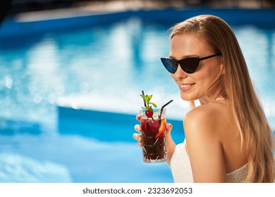 Blond Fra drénkt erfrëschende Cocktail sonnen a sëtzt bei der Schwämm am tropesche Spa. Weiblech a Sonnebrëll genéisst e Patt um Pool. Meedchen chillt am tropesche Resort an der Vakanz.