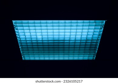 Lámparas fluorescentes azules en pantalla cuadrada con rejilla de malla celular en habitación oscura.