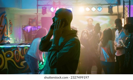 Person answering phone call at nightclub, trying to have remote conversation at disco party. Man talking on smartphone, enjoying night out at event with funky music. Handheld shot.