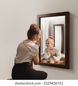 Creative conceptual collage. Young woman looking in mirror and seeing her little self. Back to childhood memories. Concept of present, past and future, age, lifestyle, emotions, generation, ad