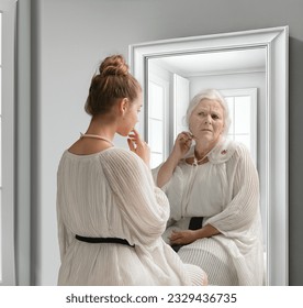 Creative conceptual collage. Young girl looking in mirror with older reflection of herself. Emotions and feelings. Look in future. Concept of present, past and future, age, lifestyle, generation, ad