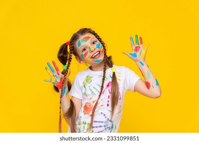 Ein mit bunten Farben bemaltes Kind. Ein junges Mädchen mit bemalten Handflächen. Kreativität für Schulkinder. Zeichnen für Kinder. Gelber isolierter Hintergrund.