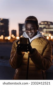 Casual African Man using cell phone to write messages and check social media in the modern city at night