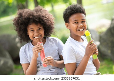 Zwee Kanner iessen Glace am Park souz op gréngt Gras.