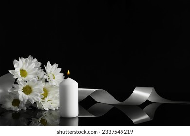 Burning candle, white chrysanthemum flowers and ribbon on black mirror surface in darkness, space for text. Funeral symbols