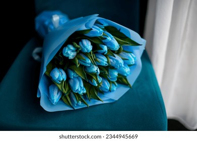 Vista frontale di uno splendido bouquet di tulipani blu avvolto in carta da imballaggio blu su una morbida sedia blu. Bouquet di fiori unico per un evento speciale