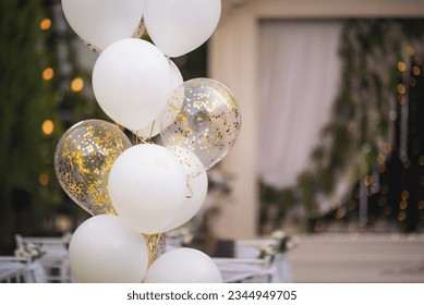 White wedding balloon. Wedding ceremony and arch decoration with white and gold balloons. Large balloons hang over white chairs. Party wedding decoration outdoor. Vintage style, flowers decoration.