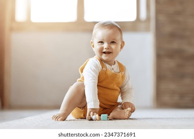 Adorable bébé blond heureux jouant avec des jouets pour enfants à la maison tout en étant assis sur un tapis dans le salon. Portrait d'un enfant mignon et souriant utilisant des jouets colorés, espace de copie