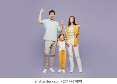 Tam vücutlu genç ebeveyn, anne, baba, çocuk, kız, 6 yaşında, mavi, sarı, gündelik kıyafetler giyiyor, kazananı kutluyor, yumruklarını sıkıyor, düz mor arka planda izole edilmiş. Aile günü konsepti