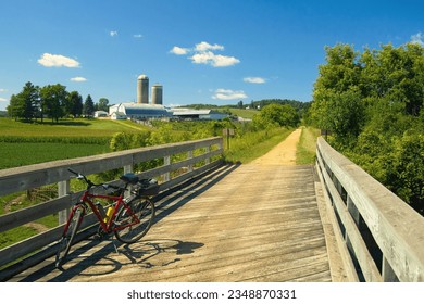 Under a blue Summer sky, a red bike rests against a wooden bridge railing on the Elroy-Sparta State Trail as it passes through farm country near Sparta, WI.