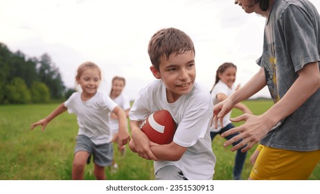 group of children run on the grass in the park with a ball. happy family childhood dream concept. children run on the green grass and play american football together. lifestyle kids have fun