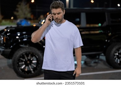 Angry man talking on phone on night urban street. Dangerous aggressive man talking on phone with serious face. Criminal city danger district. Aggressive angry man talking on phone outdoor. Night call.