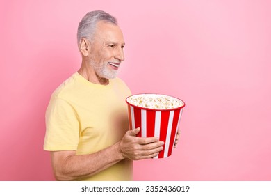 Foto eines älteren grauhaarigen alten Mannes, der leckere Chips aus dem Eimer isst und neugierig aussieht, leerer Raum, neuer Marvel-Film isoliert auf rosafarbenem Hintergrund