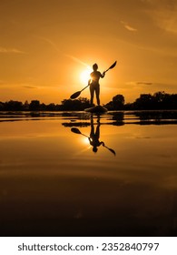 Người phụ nữ trên ván chèo đứng, chèo thuyền lúc hoàng hôn phản chiếu trên mặt nước