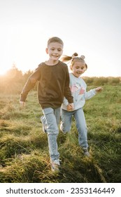 Des enfants heureux se promènent et passent du temps ensemble dans la nature. La fille et le fils se tiennent la main et courent dans l'herbe verte du champ au coucher du soleil. Concept de vacances en famille en plein air. Les enfants jouent dans les montagnes un jour d'automne.