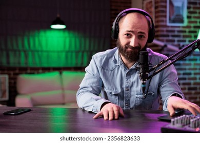 Porträt eines erfahrenen Radiomoderators, der in einem professionellen Heimstudio mit Neonlicht Musik spielt. DJ verwendet ein hochwertiges Setup, um Musikstücke zu produzieren und zu verbreiten und Fans zu unterhalten