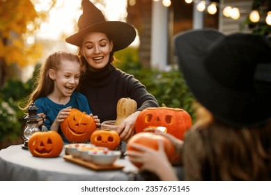 Família feliz se preparando para o Halloween. Mãe e filhos esculpindo abóboras no quintal da casa.