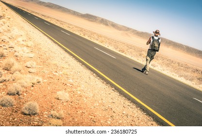 Lonely man walking along the road on namibian african desert - Alternative lifestyle concept and wanderlust experience with hipster guy backpacking to unknown - Travel trip adventure around the world