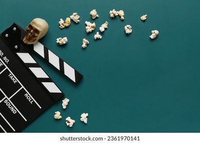 Kompositioun mat leckere Popcorn, Klapperbrett a Schädel fir Halloween Feier op gréngen Hannergrond