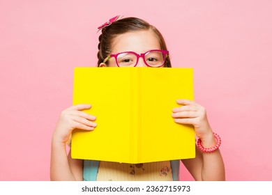 Pembe stüdyo arka planında okulda kitap okuyup ders çalışırken gözlük takan sevimli küçük kız