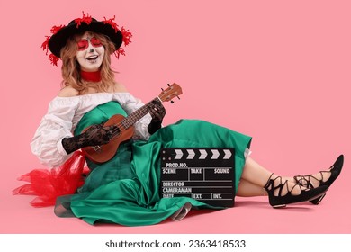 Jonk Fra mat gemooltem Schädel op hirem Gesiicht, Ukulele a Klapperbrett sëtzt géint rosa Hannergrond. Halloween Feier