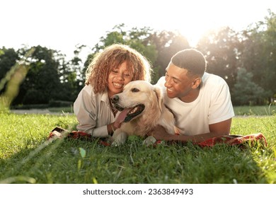 african american guy with girl lie together with golden retriever in the park in summer, young couple walks and plays with dog in nature, happy family with pet
