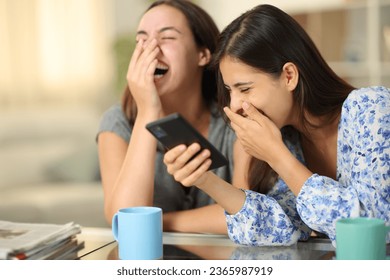 Amigos divertidos mirando medios en el teléfono riéndose a carcajadas en casa