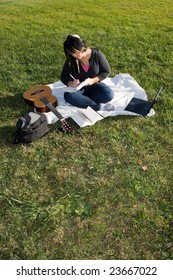 Eine junge Musikerin schreibt in ihr Notizbuch, während sie an einem schönen Tag im Gras sitzt.