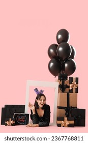Young woman with frame, shopping bags, gifts and balloons on pink background. Black Friday sale