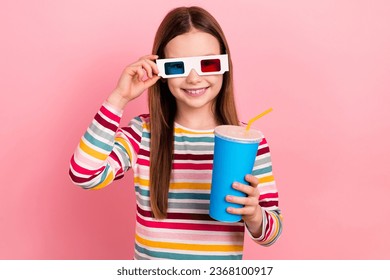Foto eines optimistischen kleinen Mädchens, das ihre 3D-Brille berührt und Cartoon Marvel Cinema Studio Drink Fanta einzeln auf rosafarbenem Hintergrund ansieht