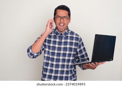 Erwuessene asiatesche Mann jäizt rosen wärend engem Telefonsgespréich beäntwert an de Laptop hält