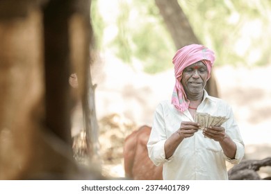 Hombre campesino de pie en el campo mostrando billetes de la India