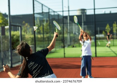 Gadis sekolah dasar yang ceria dan sporty, anak bermain bulu tangkis, memegang raket sambil membuat wajah-wajah lucu, potret, gaya hidup. Konsep rekreasi olahraga, latihan, dan aktivitas luar ruangan yang sehat, satu orang