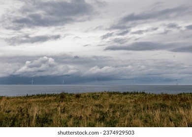 崖とドラマチックな雲が広がるイギリスの海岸沿いに、代替グリーンエネルギー用の大型洋上風車 5 基が並んでいます。高画質写真