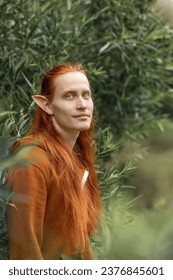 Umělecký elf muž s červenými vlasy a zelenýma očima v lese.