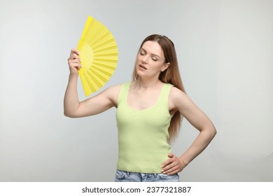 Hermosa mujer agitando un abanico amarillo para refrescarse sobre un fondo gris claro