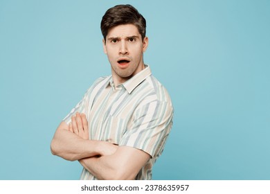 Side View jonk traureg schockéiert verréckte Mann hien huet gesträifte Shirt Casual Kleeder hält Hänn gekräizt geklappt Look Kamera isoléiert op Einfache Pastell Liichtblo Cyan Hannergrond Studioportrait. Liewensstil Konzept