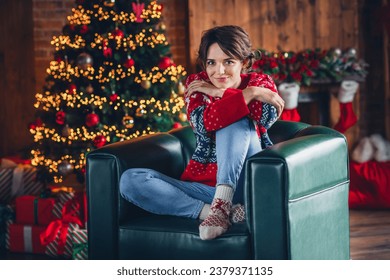 Foto de corpo inteiro de uma jovem mulher sentada em um sofá de couro verde, sonhadora, esperando o milagre da meia-noite de 2024, feliz ano novo, isolada no fundo da árvore de natal
