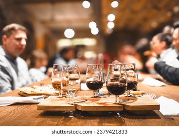 Abendessen, Weinprobe in einem alten Weingut. Elegante Weingläser mit Rot-, Weiß- und Roséweinen auf einem rustikalen Holztisch. Die Gäste unterhalten sich in gemütlicher Atmosphäre. Agrotourismus, Weingut-Event.
