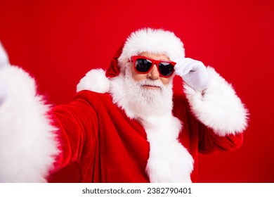 Foto de un hombre agradable y confiado, Papá Noel, blogueando, transmitiendo, filmando, celebrando una fiesta temática de Año Nuevo, aislado sobre fondo de color rojo