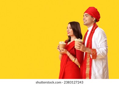 Pasangan India yang cantik dengan ember popcorn di latar belakang kuning