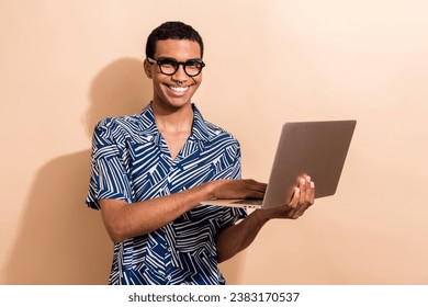 Fotografie pekného veselého úspešného muža, ktorý nosí trendy oblečenie, používa moderný gadget macbook lenovo izolovaných na béžovej farbe pozadia