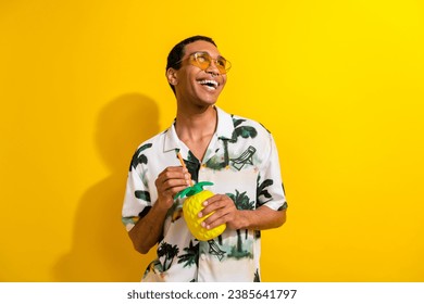 صورة لرجل إيجابي راضٍ يرتدي ملابس عصرية ويشرب عصيرًا لذيذًا وينظر إلى مساحة فارغة معزولة على خلفية باللون الأصفر
