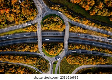 Pamje ajrore direkt mbi një kryqëzim të frekuentuar të autostradës M1 në Mbretërinë e Bashkuar me rrethrrotullim dhe mbi urë pranë Leeds me rrezet e diellit të vjeshtës dhe tendë pemësh shumëngjyrëshe